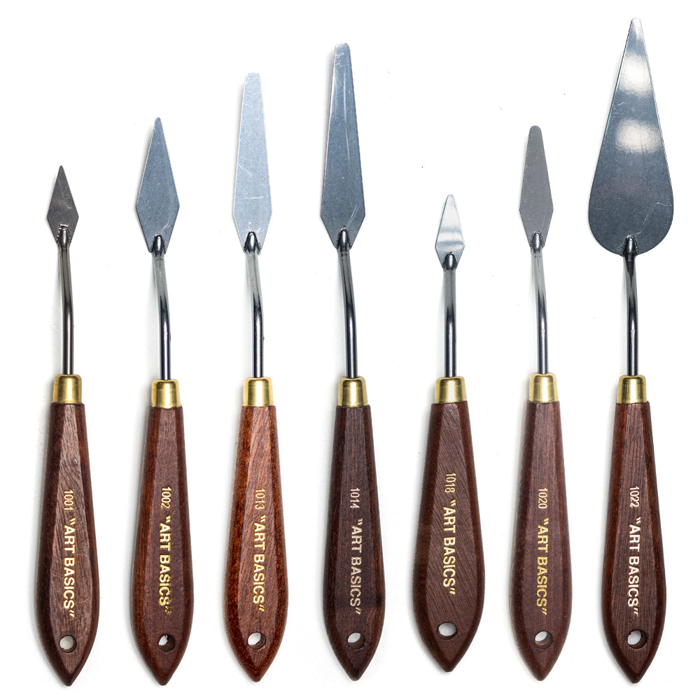 A range of Art Basics paint knives with metal blades and cranked shafts attached to wooden handles with brass ferrules.