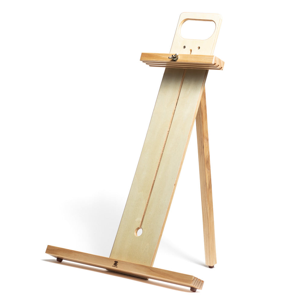 A wooden table easel with a cut out handle and an adjustable sliding top bar fixed with a wing nut. Three slots in the top and bottom bars allow for three paint boards to be carried at one time.